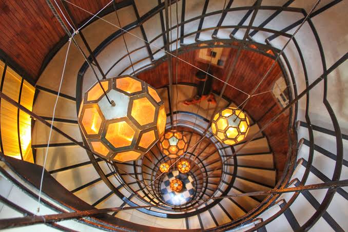 Curved stone stair rising through a panelled hall with a rail of iron