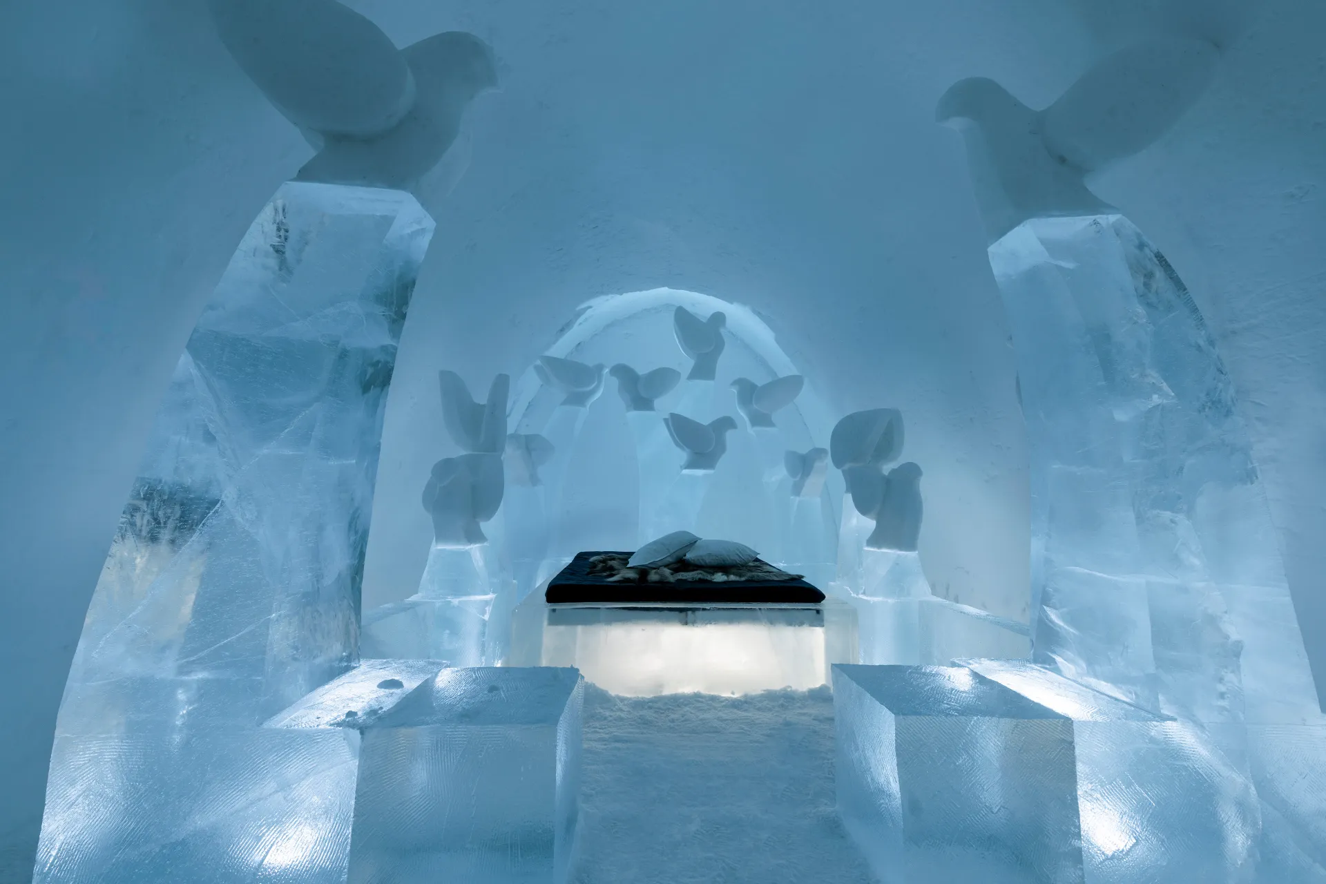 Carved wall of clear ice lit from behind inside a cold hall
