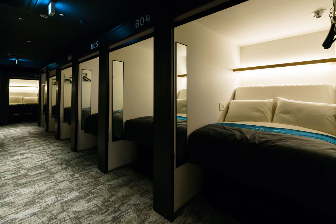 Tiered sleeping berths with pull-down screens along a lit corridor